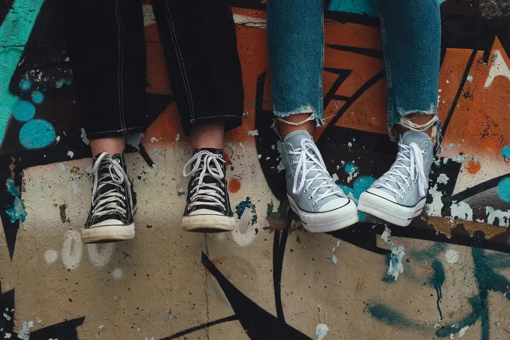 Two teens in sneakers sitting on a graffiti wall